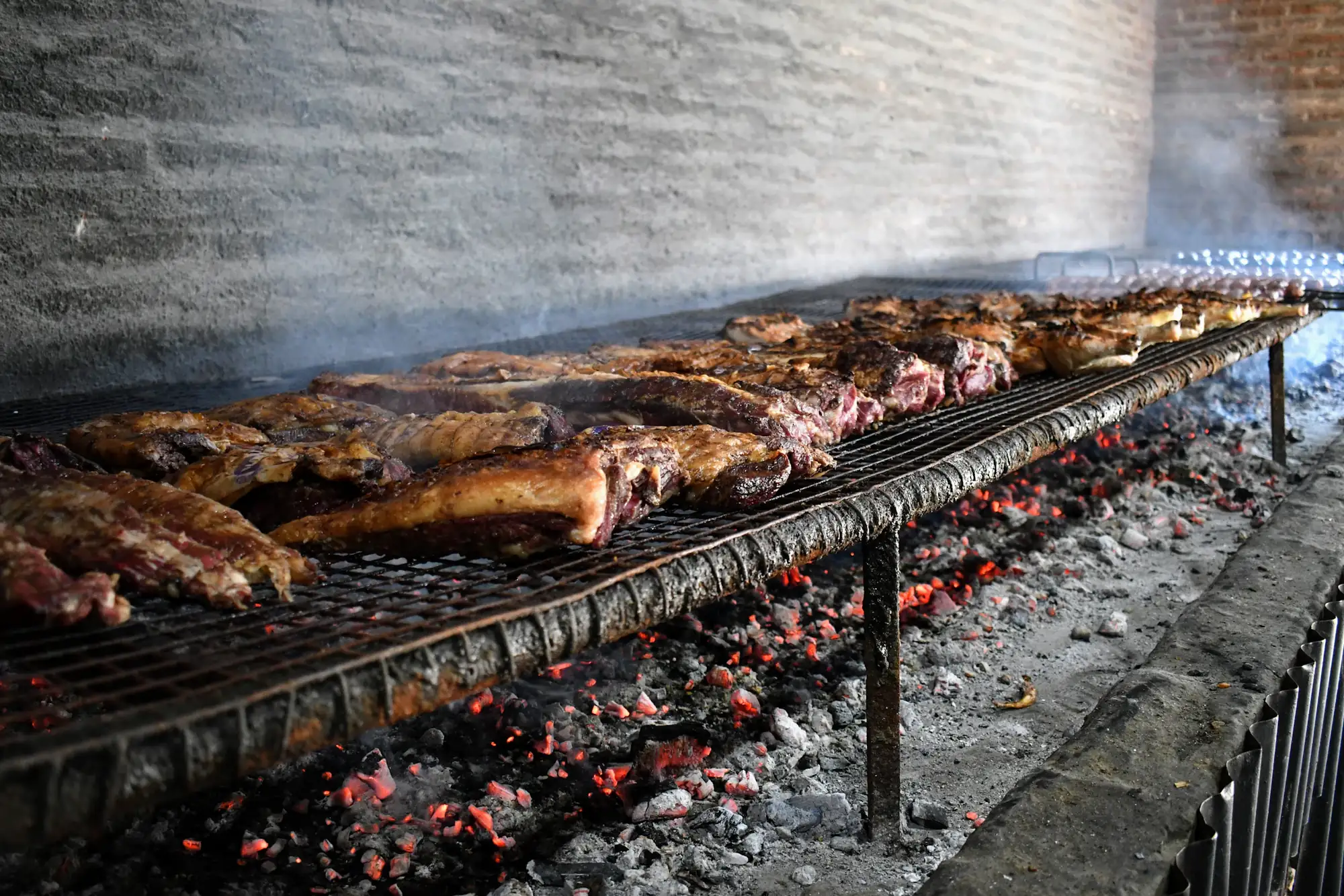 Cortes de carne asándose sobre una parrilla larga con brasas encendidas