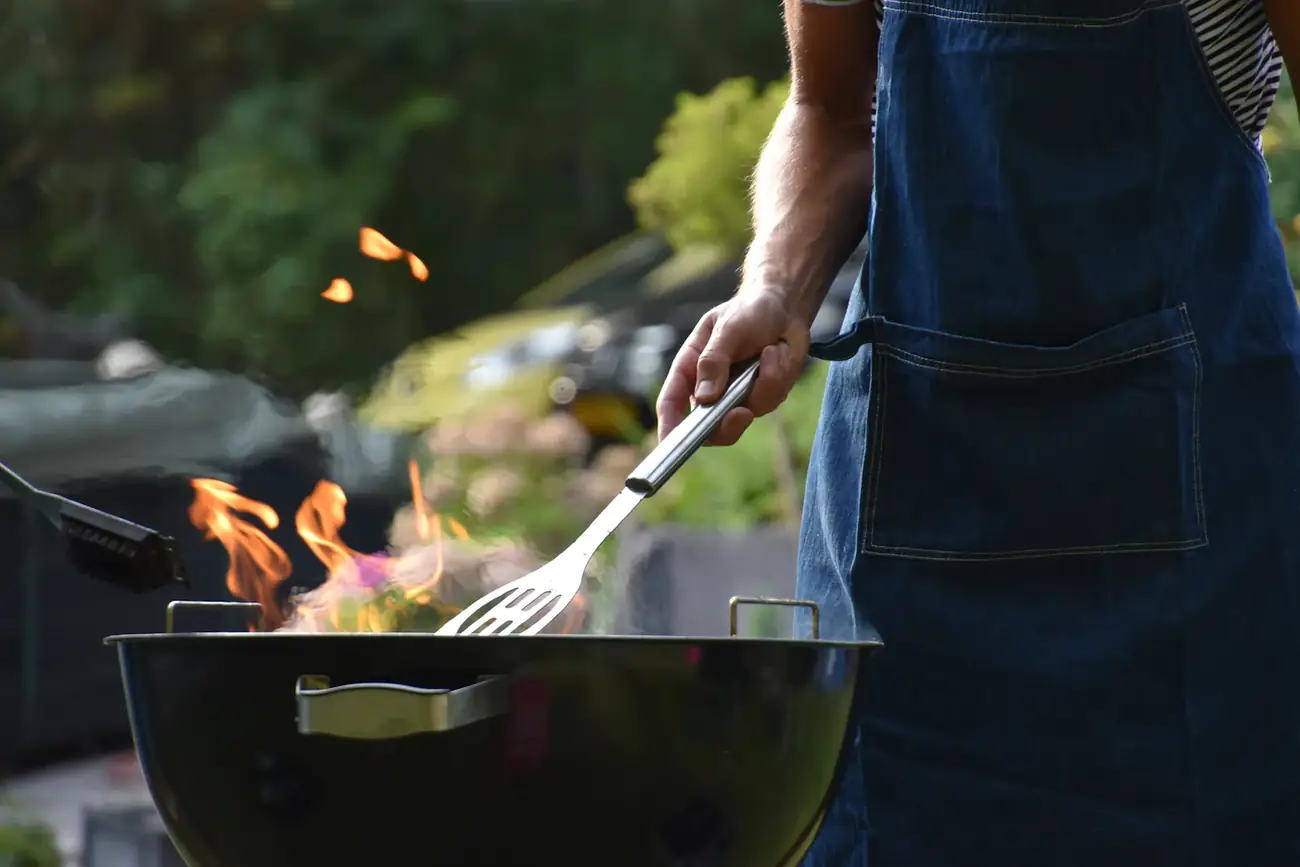 Persona con delantal asando carne sobre un asador con llamas